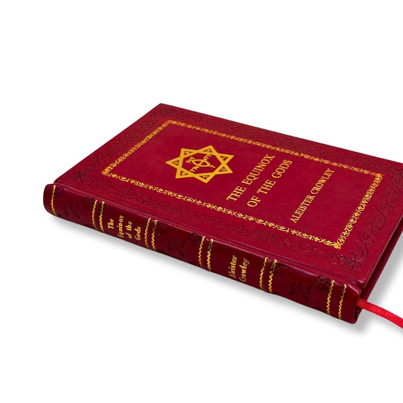 Op de afbeelding: Een rood hardcover boek getiteld "The Equinox of the Gods" van Aleister Crowley. Het boek heeft gouden letters en een gouden sterontwerp op de omslag. Een rood lint-bladwijzer is zichtbaar.