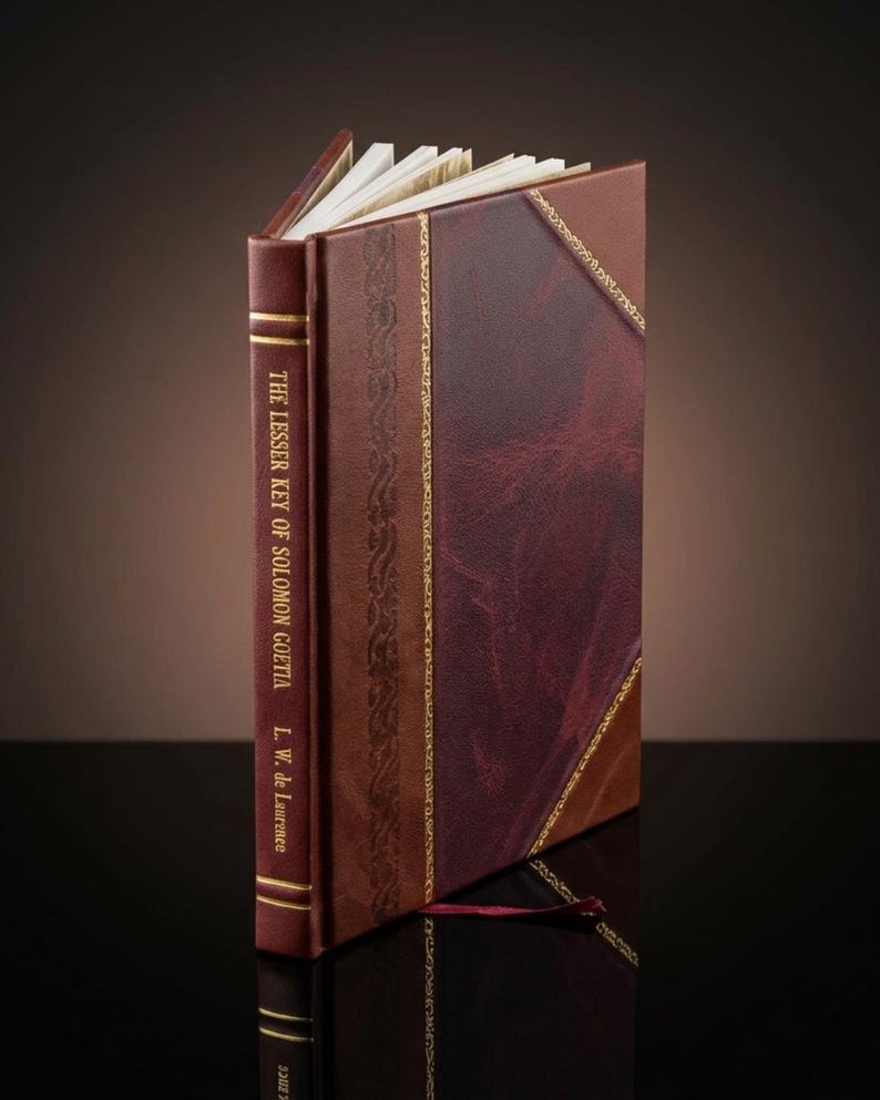 K&ouml;nnte beinhalten: Ein ledergebundenes Buch mit dem Titel "The Lesser Key of Solomon Goetia" von L.W. de Laurence. Das Buch hat einen weinroten Buchr&uuml;cken und einen braunen und weinroten Einband mit goldenen Details. Die Seiten sind sichtbar.