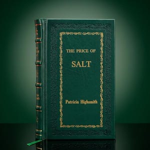 May include: A hardcover book titled "The Price of Salt" by Patricia Highsmith. The book has a dark green cover with gold lettering and decorative gold borders. A green ribbon bookmark is visible.