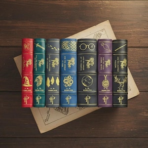Op de afbeelding: Een verzameling van zeven Harry Potter boekvormige dozen in verschillende kleuren, waaronder rood, groen en blauw. Elke doos heeft gouden illustraties en tekst, met de serietitel en de naam van de auteur. Ze liggen op een houten oppervlak met een vintage papieren.