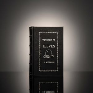 May include: A hardcover book titled "The World of Jeeves" by P.G. Wodehouse. The black book has a decorative border and a bowler hat illustration. The book is reflected on a glossy surface.