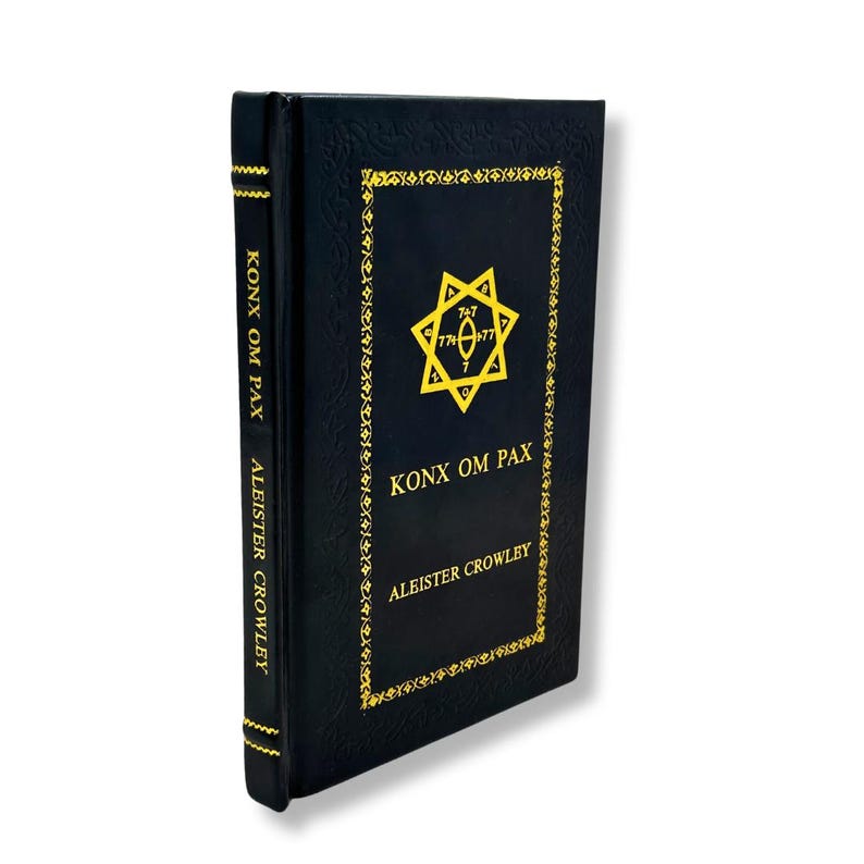 Peut inclure: Livre &agrave; couverture rigide noire intitul&eacute; "Konx Om Pax" d'Aleister Crowley. Le titre et les motifs g&eacute;om&eacute;triques sont dor&eacute;s. La tranche du livre porte &eacute;galement des inscriptions dor&eacute;es. L'arri&egrave;re-plan est blanc.