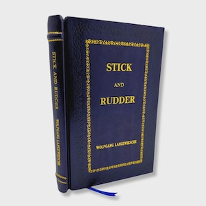 Puede incluir: Un libro de tapa dura azul oscuro titulado "Stick and Rudder" de Wolfgang Langewiesche. La portada tiene letras doradas y un borde dorado decorativo. Se ve una cinta azul como marcapáginas.