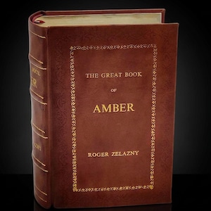 May include: A hardcover book titled "THE GREAT BOOK OF AMBER" by Roger Zelazny. The book has a brown leather cover with gold lettering and decorative border. A red ribbon bookmark is visible.
