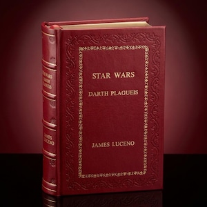 Op de afbeelding: Een rood hardcover boek getiteld "Star Wars Darth Plagueis" van James Luceno. De kaft heeft gouden letters en decoratieve randen. De rug van het boek toont ook de titel en de naam van de auteur.