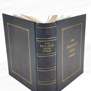 Puede incluir: Un libro de tapa dura con cubierta negra y detalles dorados. El lomo muestra "THE PROLOGUE FROM OHRID" en dorado. El libro est&aacute; abierto, mostrando las p&aacute;ginas.