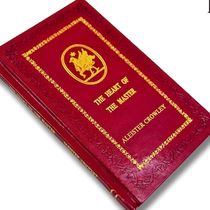 Könnte beinhalten: Ein rotes Hardcover-Buch mit dem Titel "The Heart of the Master" von Aleister Crowley. Das Cover zeigt goldene Schrift und ein goldenes Emblem. Das Buch hat dekorative goldene Ränder und geprägte Details.