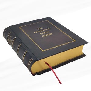 Puede incluir: Un libro de tapa dura con el t&iacute;tulo "THE PROLOGUE FROM OHRID" en letras doradas. El libro tiene una cubierta negra con adornos dorados y cantos dorados. Una cinta roja de marcador se extiende desde las p&aacute;ginas.