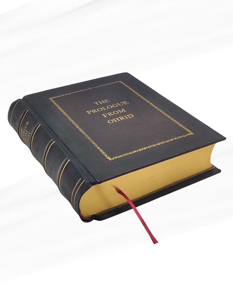 Puede incluir: Un libro de tapa dura con el t&iacute;tulo "THE PROLOGUE FROM OHRID" en letras doradas. El libro tiene una cubierta negra con adornos dorados y cantos dorados. Una cinta roja de marcador se extiende desde las p&aacute;ginas.