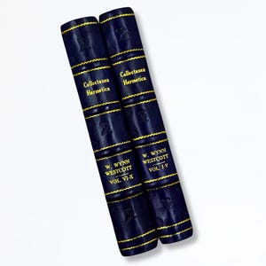 May include: Two navy blue leather-bound books with gold lettering and detailing. The spines display the titles "Collectanea Hermetica" and "W. Wynn Westcott, Vol. VI-X" and "Vol. I-V". The books have gold trim.