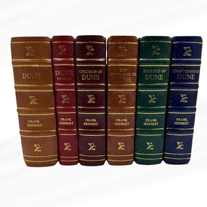 Könnte beinhalten: Sechs gebundene Bücher mit goldener Schrift. Die Buchrücken zeigen Titel wie "Dune" und "Heretics of Dune" von Frank Herbert. Die Bücher sind in Braun-, Burgunder-, Grün- und Blautönen gehalten und mit Gold verziert.