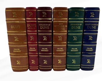 May include: A collection of six hardcover books with gold lettering and accents. The spines display titles like "Dune" and "Children of Dune" by Frank Herbert. The books are in various colors, including brown, burgundy, green, and blue.