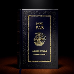 Op de afbeelding: Een donkerblauw hardcover boek getiteld "DARK FAE" met gouden letters en accenten. De omslag heeft een weegschaal en een halve maan ontwerp. De namen van de auteurs staan ook in goud.
