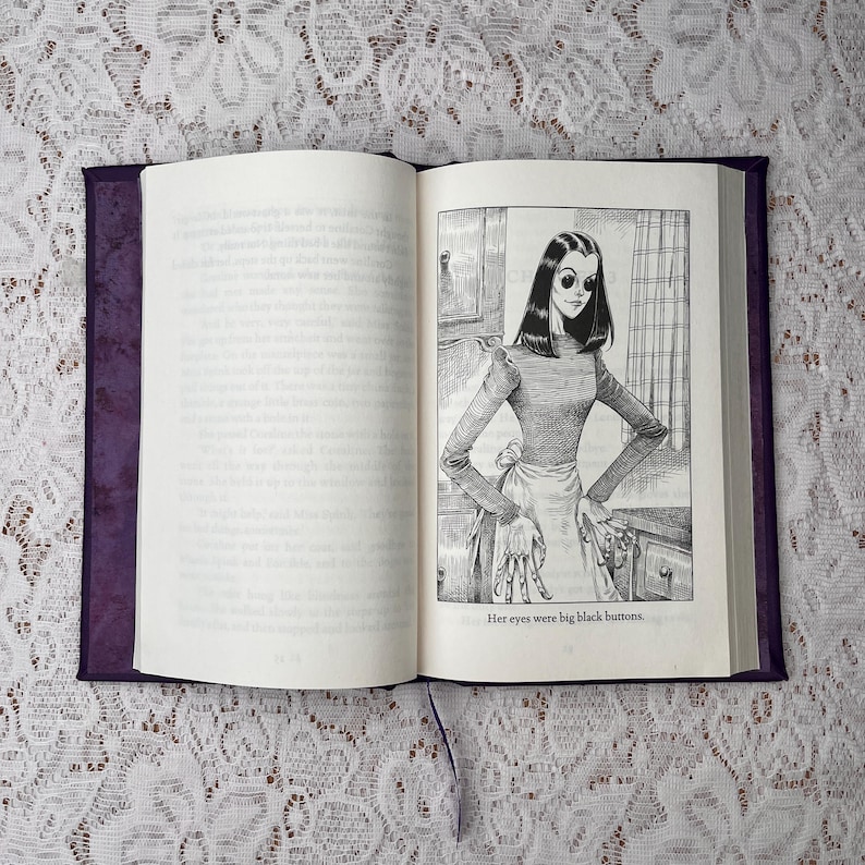May include: An open book with a purple cover and a ribbon bookmark. The right page features a black and white illustration of a woman with large black eyes, wearing a long-sleeved top and apron. The text reads, "Her eyes were big black buttons."