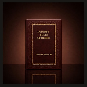 May include: A dark brown hardcover book titled Robert's Rules of Order by Henry M. Robert III. The front cover features a gold embossed rectangular border with intricate decorative patterns and gold lettering centered on the front surface.
