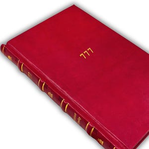Op de afbeelding: Een rood hardcover boek met gouden letters en details. Het nummer "777" is in goud op de omslag gedrukt. De rug heeft gouden accenten en de naam van de auteur. De omslag van het boek is een diep, rijk rood.