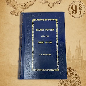 Op de afbeelding: Een blauw hardcover boek getiteld "Harry Potter en de Vuurbeker" van J.K. Rowling. De omslag heeft gouden letters en decoratieve randen. De afbeelding bevat illustraties van een uil, een gouden snaai en het nummer 9 3/4.