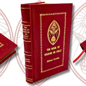 Könnte beinhalten: Ein rot gebundenes Buch mit dem Titel "The Book of Wisdom or Folly" von Aleister Crowley. Das Cover zeigt goldgeprägten Text und ein detailliertes Emblem. Der Buchrücken hat ebenfalls goldene Schrift. Ein rotes Lesezeichen ist sichtbar.