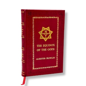 Op de afbeelding: Een rood hardcover boek getiteld "The Equinox of the Gods" van Aleister Crowley. Het boek heeft gouden letters en een decoratieve rand. Een gouden embleem staat in het midden van de voorkant, met een rood lint als boekenlegger.