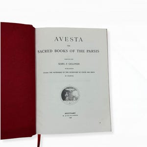 Op de afbeelding: Een open boek met een rode kaft en witte pagina's. De titel "AVESTA" staat bovenaan, gevolgd door "THE SACRED BOOKS OF THE PARSIS". De tekst is bewerkt door Karl F. Geldner en gepubliceerd onder de bescherming van de Staatssecretaris voor India.