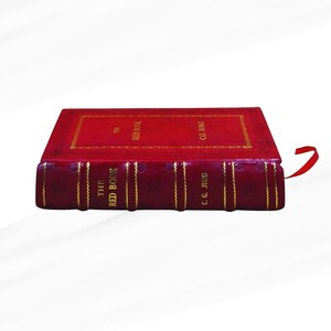 Op de afbeelding: Een rood hardcover boek getiteld "The Red Book" van C.G. Jung. Het boek heeft gouden letters en details. Een rood lint als boekenlegger is zichtbaar. Het boek staat tegen een witte achtergrond.