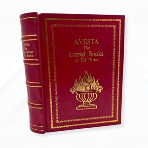 Op de afbeelding: Een decoratief rood boek met gouden letters en een gouden rand. De titel luidt "AVESTA The Sacred Books of The Parsis." De rug is rood met gouden lijnen en de tekst "AVESTA The Books of The Parsis."