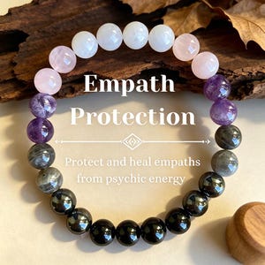 Puede incluir: Una pulsera de cuentas con piedras preciosas blancas, rosas, moradas y negras. La pulsera muestra el texto "Empath Protection" y "Protect and heal empaths from psychic energy".