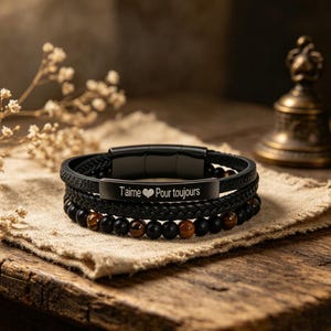 May include: A stack of three black bracelets. The top bracelet is braided leather with a magnetic clasp. The middle bracelet has a black metal plate with the words "T'aime Pour toujours" and a heart symbol. The bottom bracelet has black and brown beads.