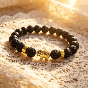 Puede incluir: Pulsera de cuentas de piedra de lava negra con un dije y detalles dorados de elefante. La pulsera presenta cuentas negras redondas y texturizadas y un dije de elefante detallado. Los detalles dorados añaden elegancia a la pulsera.