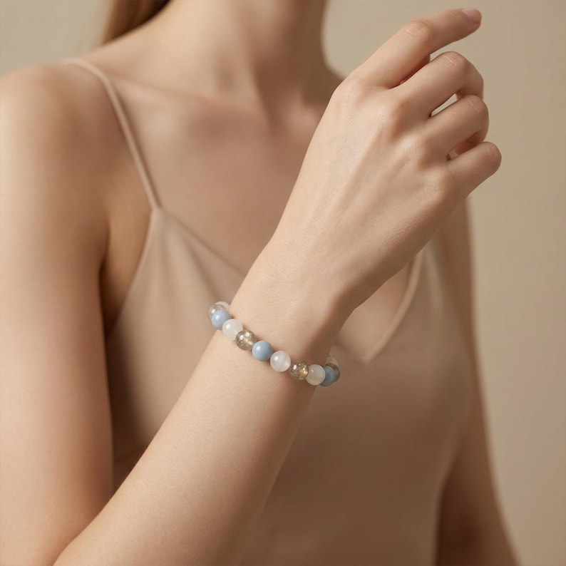 May include: A beaded bracelet featuring light blue, white, and gold-colored spherical beads. The bracelet is worn on a wrist, with the beads appearing to be approximately 0.5 inches in diameter. The bracelet is a piece of jewelry.