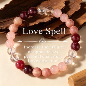 May include: A beaded bracelet with pink, clear, and dark red stones. The text "Love Spell" is above the bracelet, with additional text below describing the bracelet's properties. The bracelet is displayed on a brown surface.