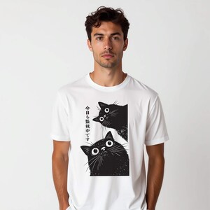 Pu&ograve; includere: T-shirt bianca con una grafica nera di due gatti con grandi occhi. Il testo giapponese sul lato sinistro della maglietta recita "Stiamo guardando anche oggi."