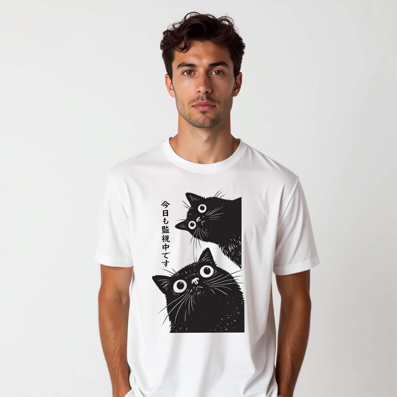 Pu&ograve; includere: T-shirt bianca con una grafica nera di due gatti con grandi occhi. Il testo giapponese sul lato sinistro della maglietta recita "Stiamo guardando anche oggi."