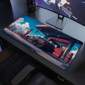 May include: A rectangular desk mat featuring a vibrant illustration of a black sports car parked at an auto service station. A figure in a red racing suit stands nearby under a bright blue sky with clouds. The scene includes red fuel pumps.