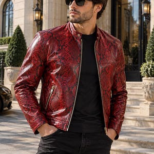 May include: A red and black snakeskin-patterned leather jacket with a mandarin collar, a full-length silver front zipper, and two zippered side pockets, worn over a plain black t-shirt and dark jeans with black sunglasses.