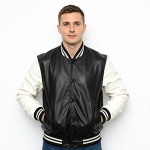 May include: A black and white varsity jacket with a leather-like appearance. The jacket features a black body, white sleeves, and black and white striped details on the collar, cuffs, and hem. It has a button-up front and two front pockets.