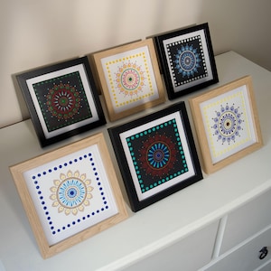Peut inclure: Six impressions d'art carrées encadrées avec des motifs de mandala. Les impressions présentent des motifs de points colorés dans diverses combinaisons de couleurs, notamment le rouge, le bleu, le jaune et le vert, sur des fonds noirs et blancs. Les cadres sont noirs ou en bois naturel.