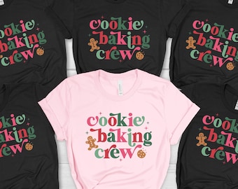May include: A collection of black and pink t-shirts with the text "Cookie Baking Crew" in a retro font. The design includes a gingerbread man and a cookie. The shirts are short-sleeved and suitable for a holiday theme.