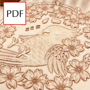 Può includere: Un'intagliatura in pelle marrone chiaro dettagliata con un uccello circondato da fiori in fiore. L'uccello è a riposo, con le sue ali e piume intagliate in modo intricato. I fiori sono in piena fioritura, aggiungendo al tema naturale. La parola "PDF" è in una casella bianca.