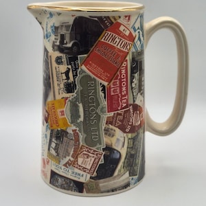 May include: A cream-colored ceramic pitcher featuring a collage of vintage Ringtons Ltd. tea and coffee advertisements, including text such as Ringtons Tea, Coffee & Chicory Essence, and Free to You, with a gold-trimmed rim and a curved handle.