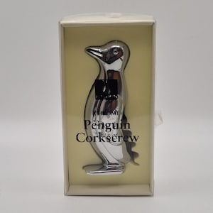 May include: A chrome penguin corkscrew in a clear box. The penguin-shaped corkscrew has a shiny, reflective surface. The text "Chrome Penguin Corkscrew" is printed on the box in black letters.