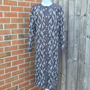 May include: A long-sleeved, knee-length dress in a dark navy blue fabric featuring a repeating white leaf pattern. The garment has a round neckline and a full-length front button placket with small, light-colored circular buttons running from the neck to the hem.