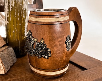 Könnte beinhalten: Ein hölzerner Bierkrug mit Griff und dekorativen Metallakzenten. Der Krug ist braun mit einem Edelstahl-Innenraum. Eine grüne Flasche mit Kerzenwachs und Brennholz sind ebenfalls im Bild.