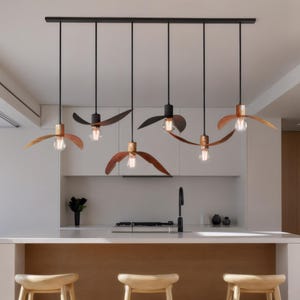Peut inclure: Six lampes suspendues au design unique sont suspendues à une barre noire. Chaque lampe est dotée d'une ampoule avec un abat-jour en forme d'éventail en bois ou marron foncé. Les lampes sont suspendues au-dessus d'un îlot de cuisine avec des tabourets en bois.