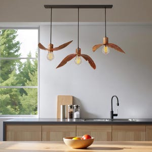 Puede incluir: Tres lámparas colgantes con un diseño único. Cada lámpara presenta una pantalla en forma de hoja de color cobre que rodea una bombilla de estilo vintage. Las lámparas están suspendidas de una barra oscura y rectangular, creando un ambiente cálido en una cocina.