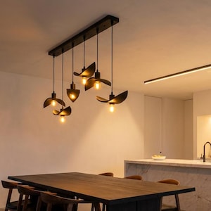 May include: Modern dining room with a dark wood table and chairs. Above the table, a unique light fixture with six black, petal-shaped shades hangs. A marble-topped island and linear lighting complete the contemporary design.