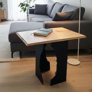 May include: A modern living room with a gray sectional sofa, wooden coffee table, and a floor lamp. The coffee table has a natural wood top and black metal base. A notebook rests on the table. The room has light-colored hardwood floors and sheer curtains.