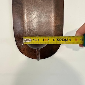 May include: A copper-colored, teardrop-shaped metal object with a small stem. A measuring tape shows the object is approximately 4 inches long. The object has a textured surface and appears to be a decorative item.