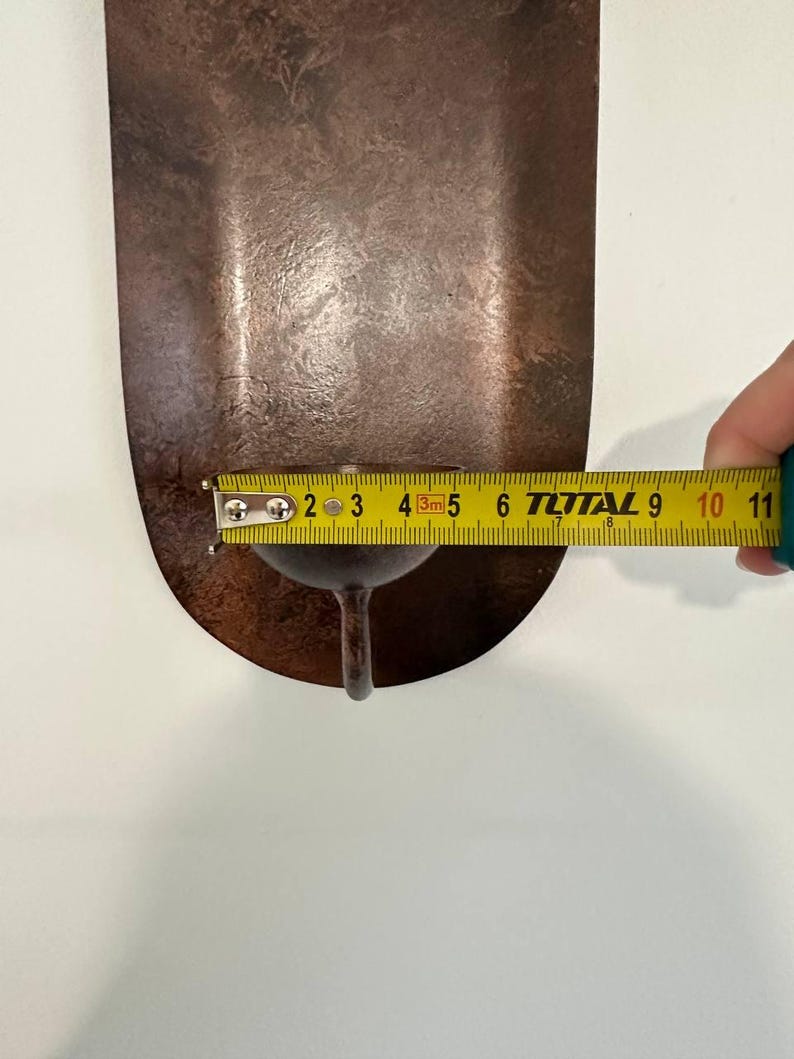 May include: A copper-colored, teardrop-shaped metal object with a small stem. A measuring tape shows the object is approximately 4 inches long. The object has a textured surface and appears to be a decorative item.