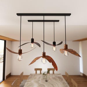May include: Five-light pendant light fixture with a black rectangular base. Each light has a rusty brown, leaf-shaped shade and a clear Edison-style bulb. The fixture hangs from the ceiling in a dining room.